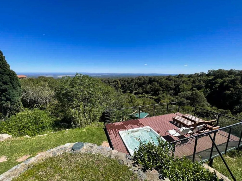 Respiro a lo ancho antes del listado: el deck con hidromasaje y reposeras sobre la ladera, con el monte y el llano abajo